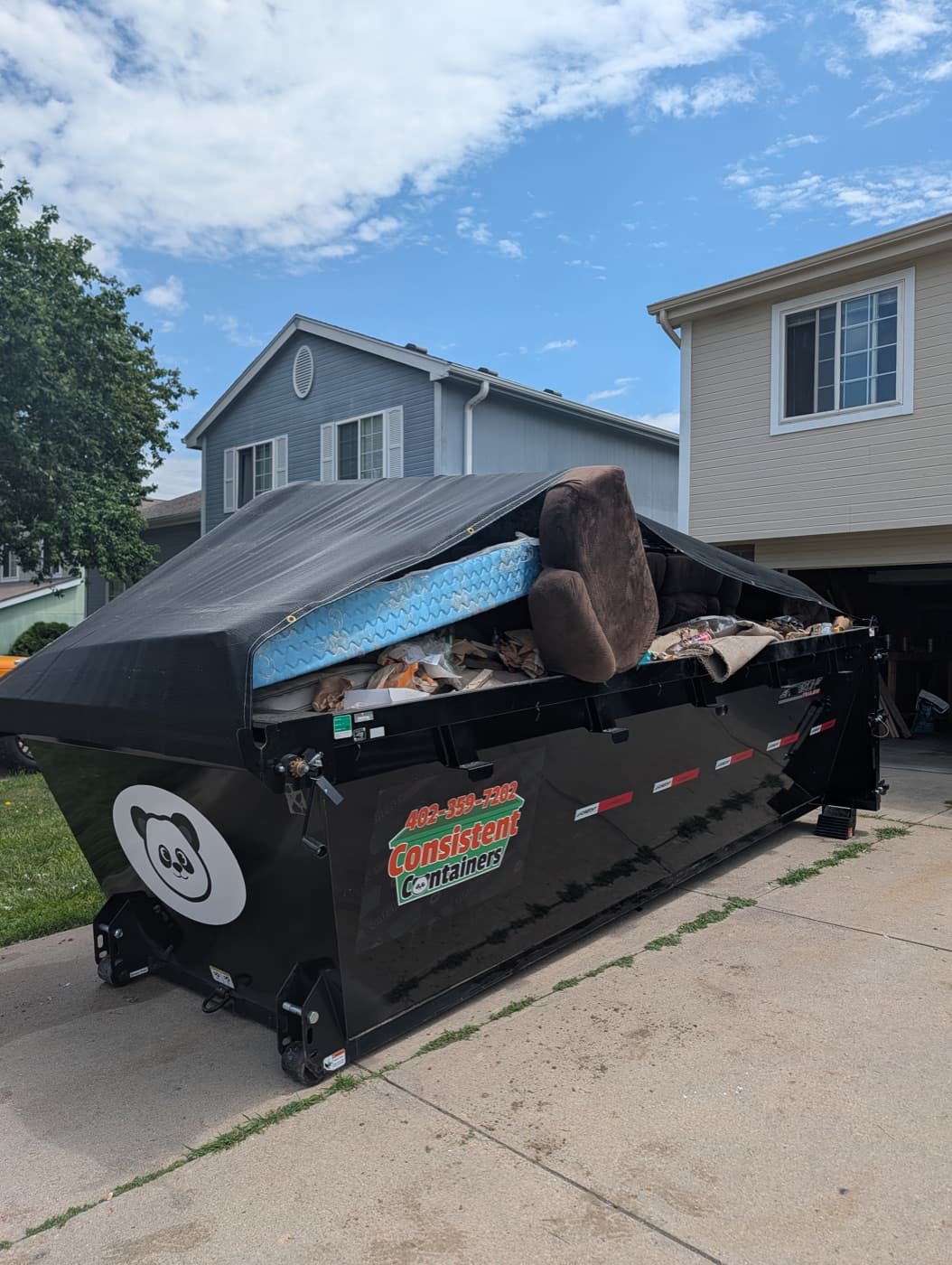 A roll-off dumpster filled with a mattress, couch, and household junk outside an Omaha home